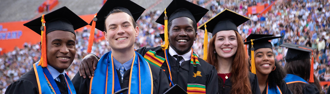 毕业时穿着帽子和礼服微笑的五个学生。