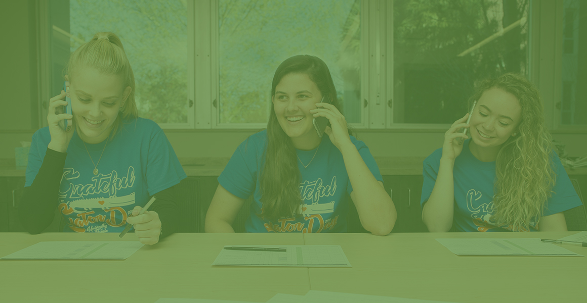 坐在桌子旁的三名女性CAL学生在手机上打电话给学生慈善委员会的潜在捐助者。 