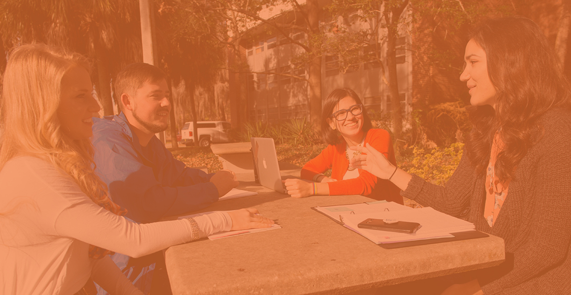 四名Cals学生坐在外面的背包和功课的外面桌子上说话。 